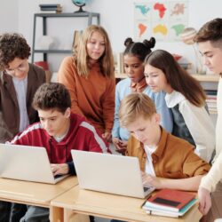 A group of middle school students gathering around a laptop